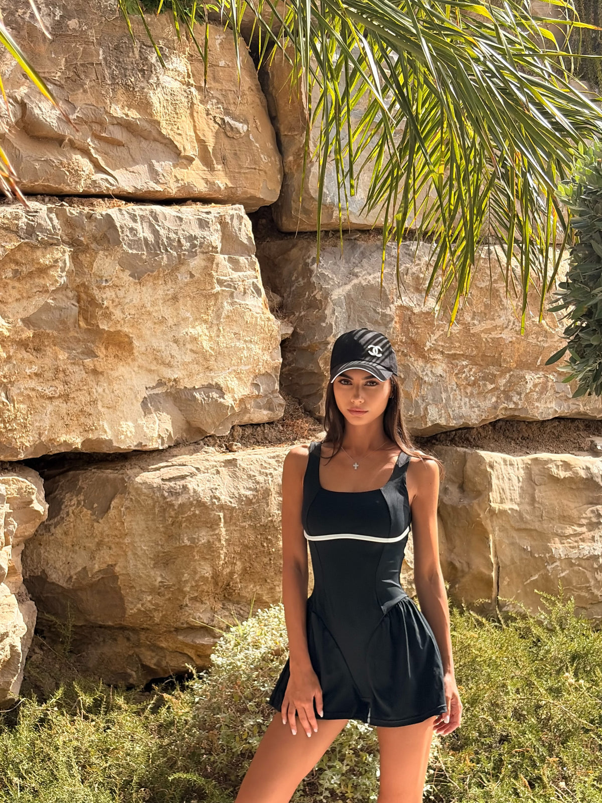 Model in the Solé dress in black beside a striped beach cabin