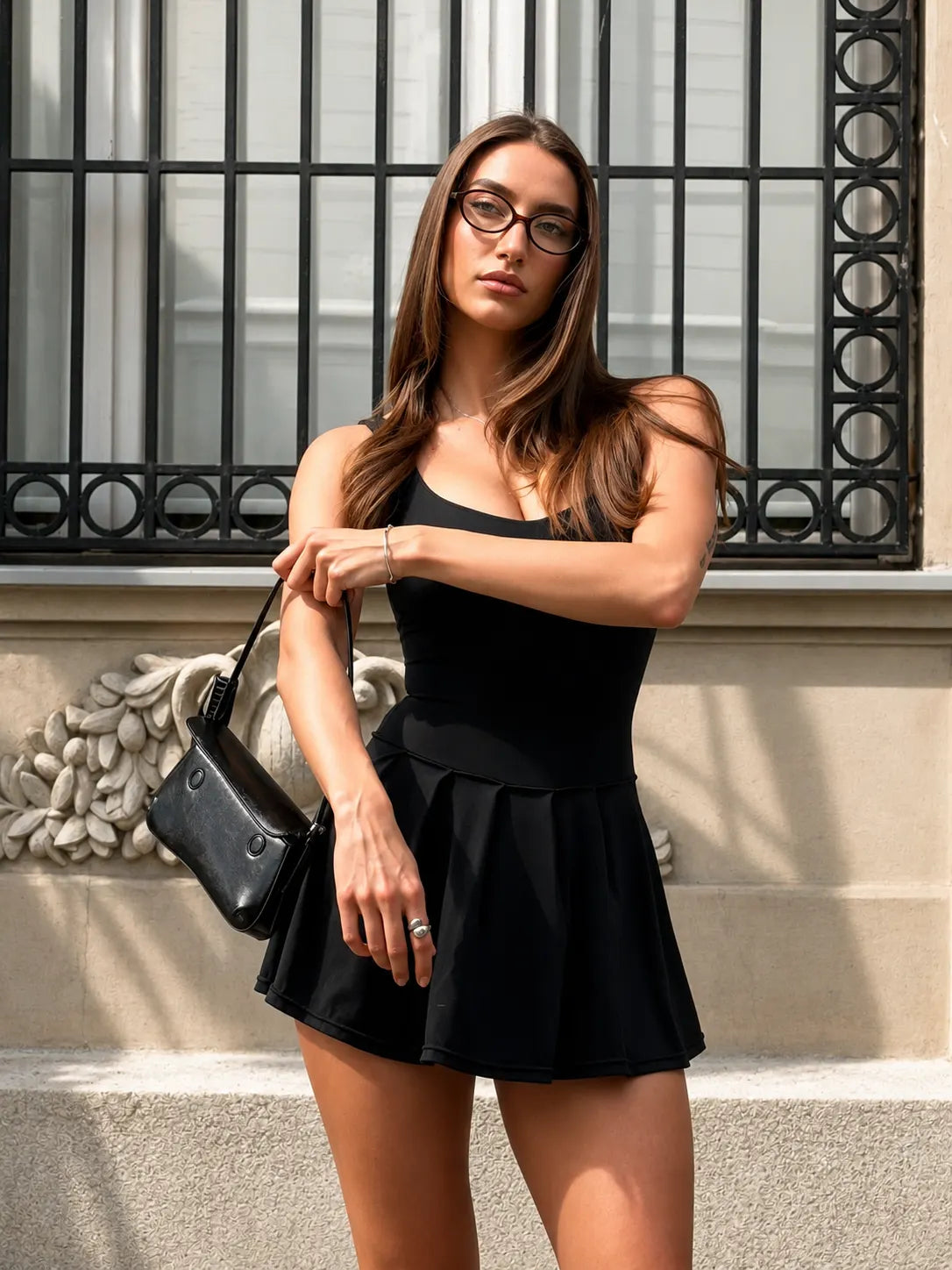 Model in a black MALU dress on a city street, carrying the MALU shoulder bag